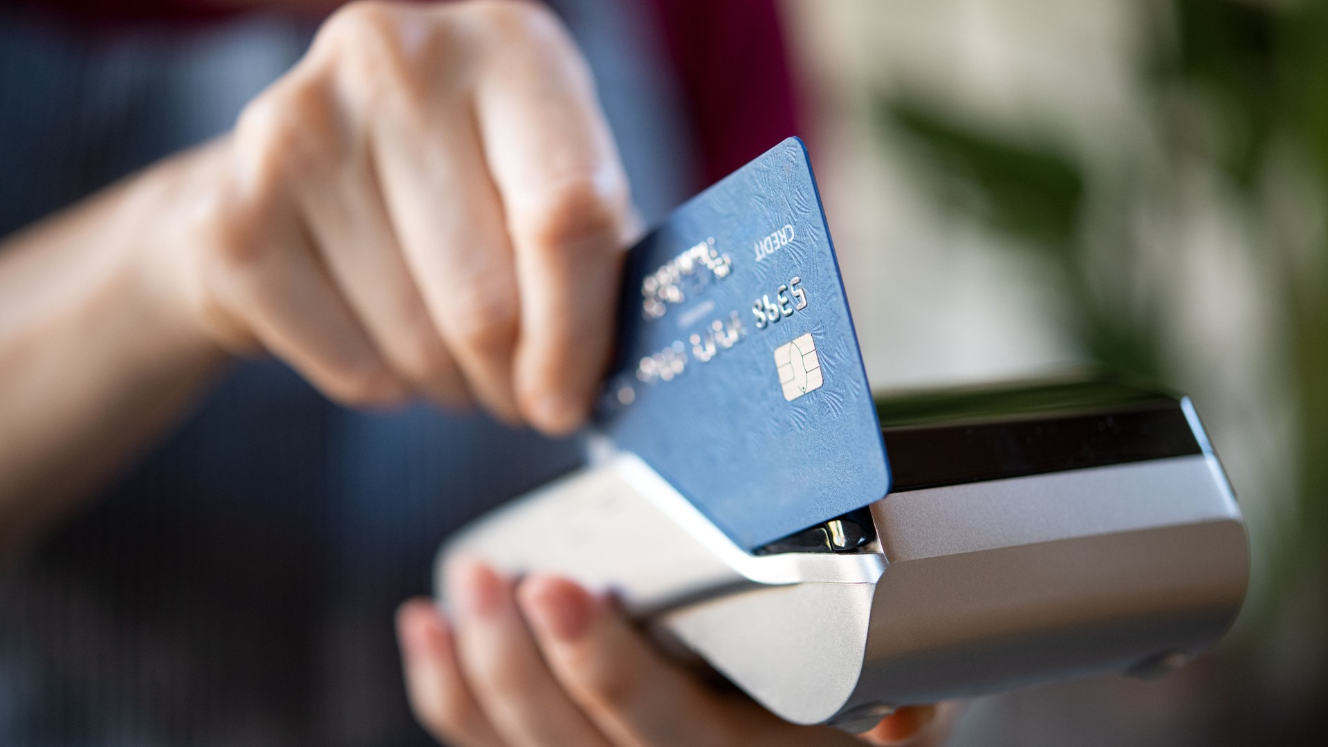 Close-up of a hand inserting a blue credit card into a payment terminal.